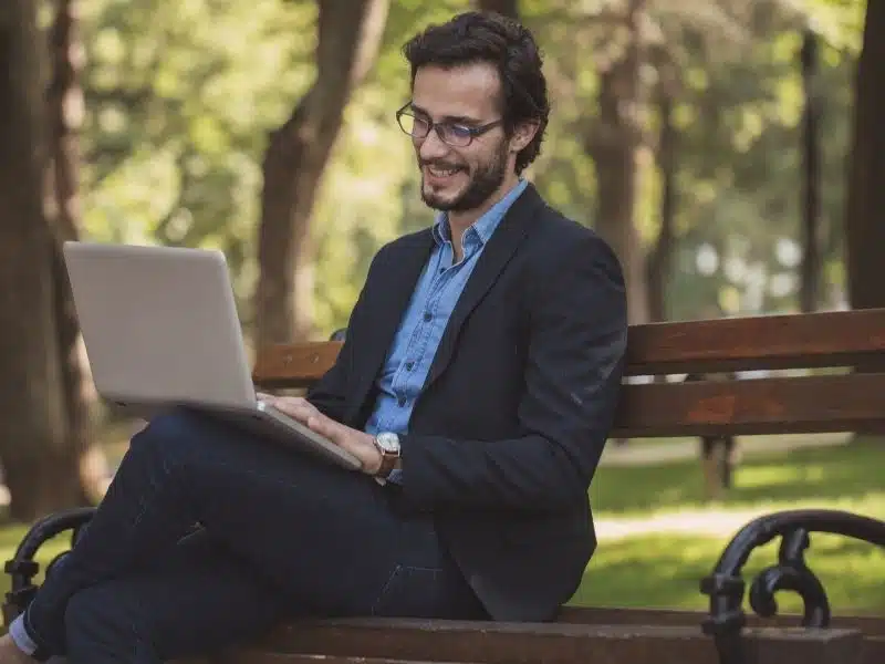 A picture of a man sitting on a bench and working on a laptop